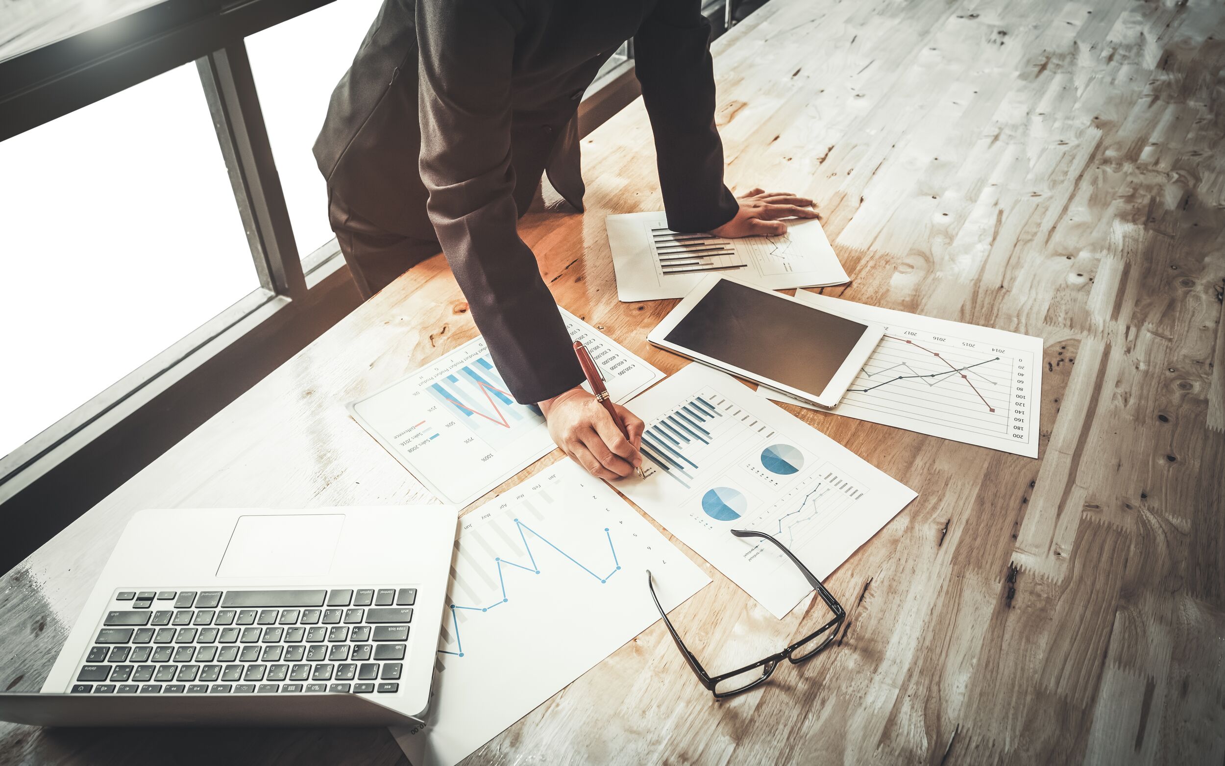Files, glasses and a laptop on a desk.